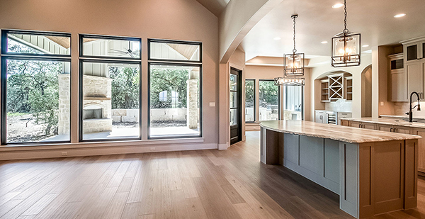 Open-concept kitchen and living space featuring custom cabinetry, large picture windows, designer lighting, and natural light throughout.