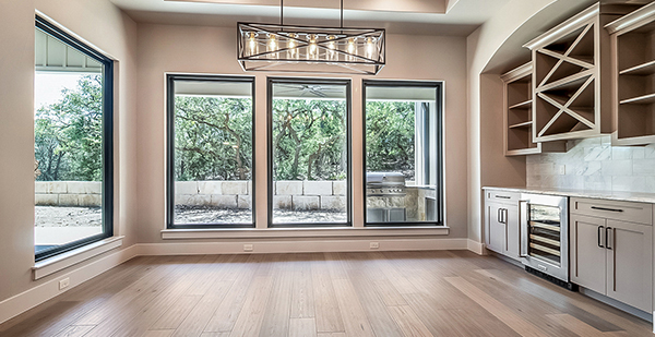 Spacious living room with vaulted ceilings, exposed beams, oversized windows, and seamless flow into the gourmet kitchen in a Texas Hill Country custom home.