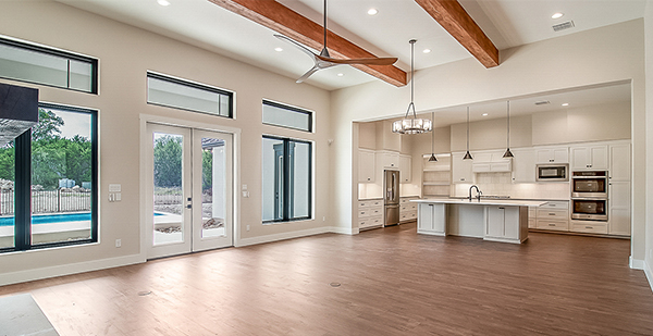 Bright great room with expansive windows, wood beam accents, custom lighting, and open-concept kitchen in Boerne, Texas